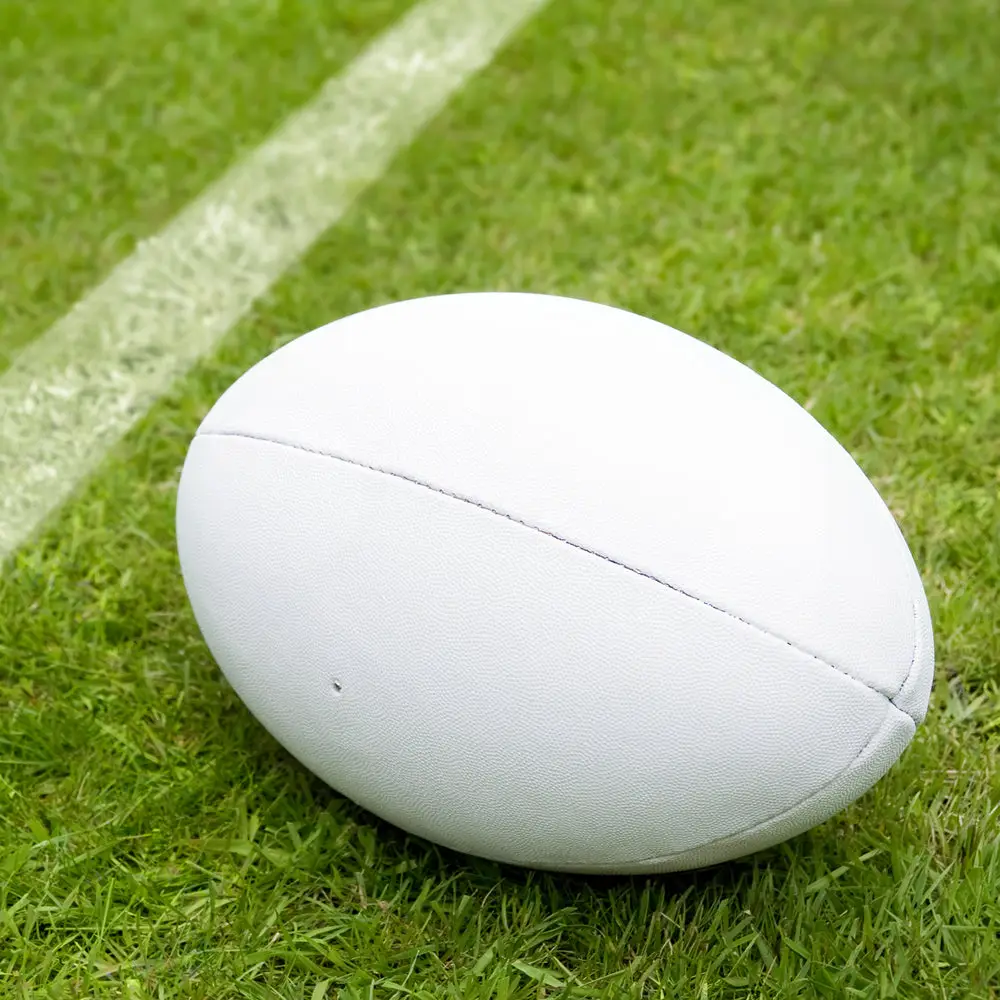 White rugby ball resting beside a freshly marked boundary line on a green grass sports field.