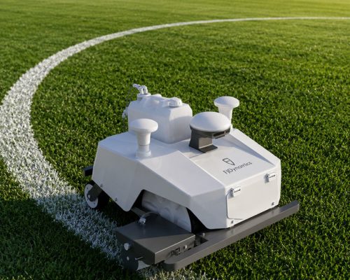 Autonomous sports field line-marking robot painting a precise curved white boundary line on green grass.